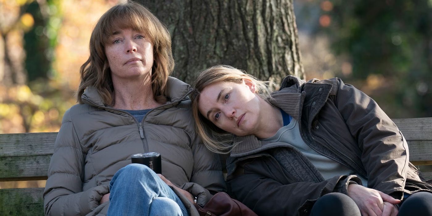 Julianne Nicholson sitting on a park bench with Kate Winslet's head on her shoulder in 'Mare of Easttown'