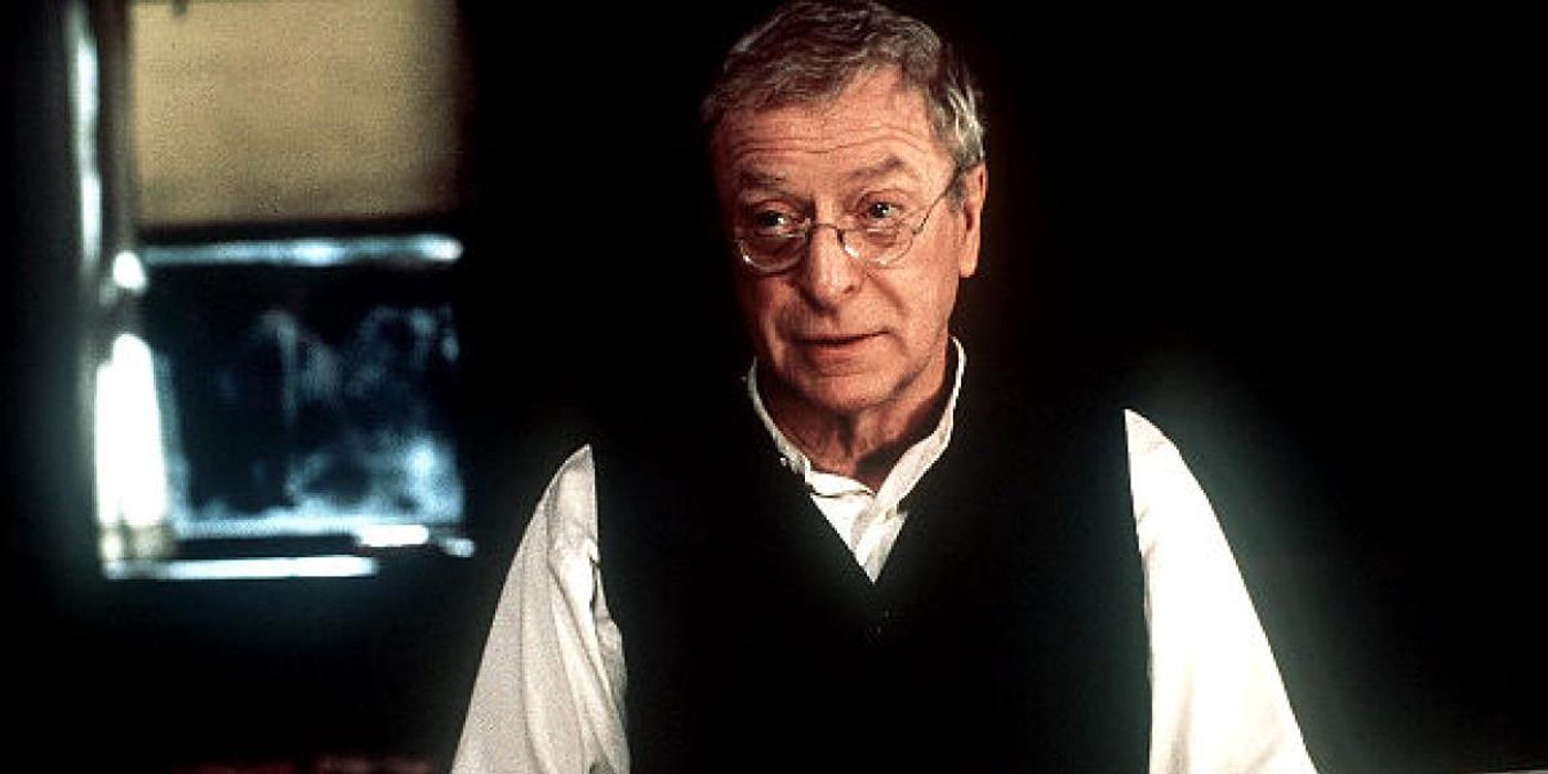 Michael Caine standing in an old house wearing glasses in 'The Cider House Rules'.