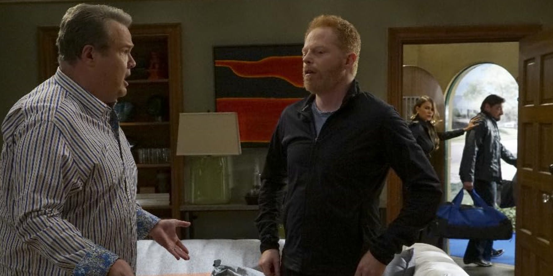 Cam (Eric Stonestreet) talking to  Mitch (Jesse Tyler Ferguson) as Gloria (Sofía Vergara) sneaks someone out in Modern Family