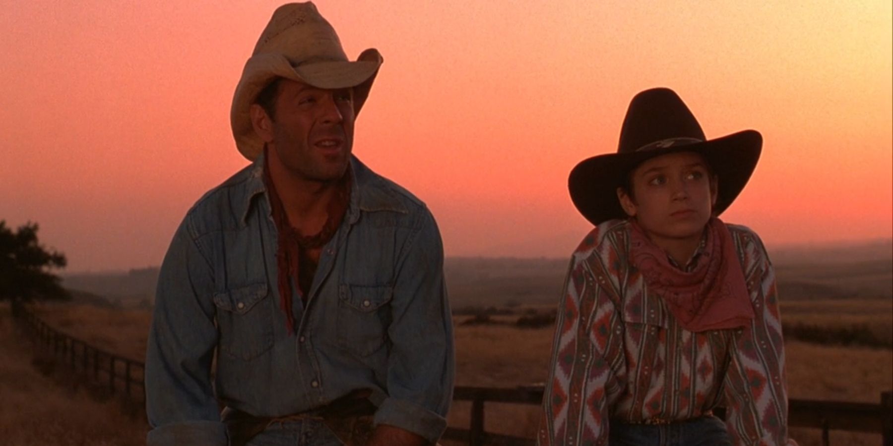 Gabby, played by Bruce Willis, sits by North, played by Elijah Wood, both in cowboy attire in 'North'.