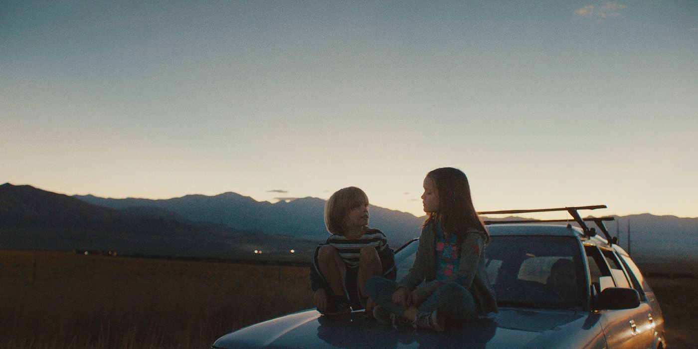 Charlie (Wyatt Solis) and Ella (Molly Belle Wright) sitting on the hood of a car as the sun sets in Omaha