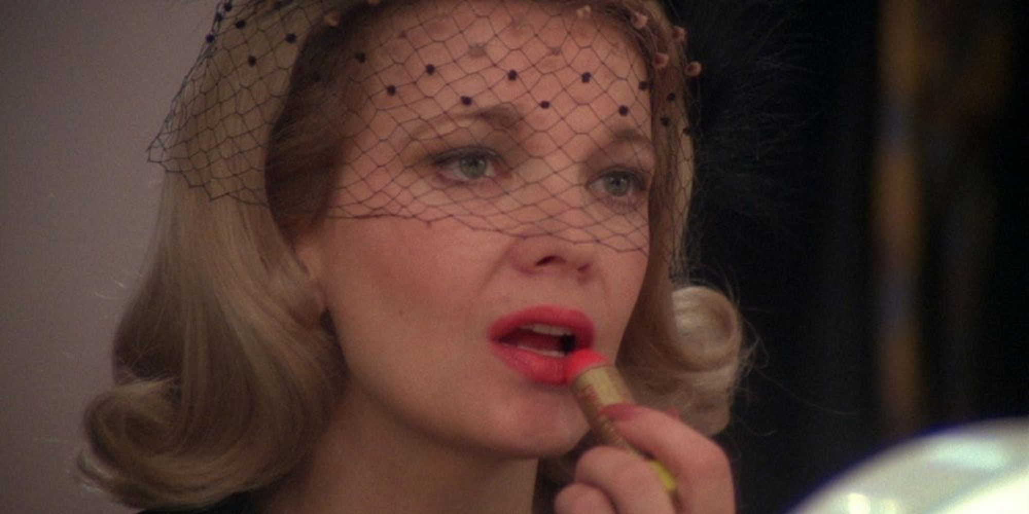 Myrtle, played by actor Gena Rowlands, applies lipstick while wearing a black veil in Opening Night.
