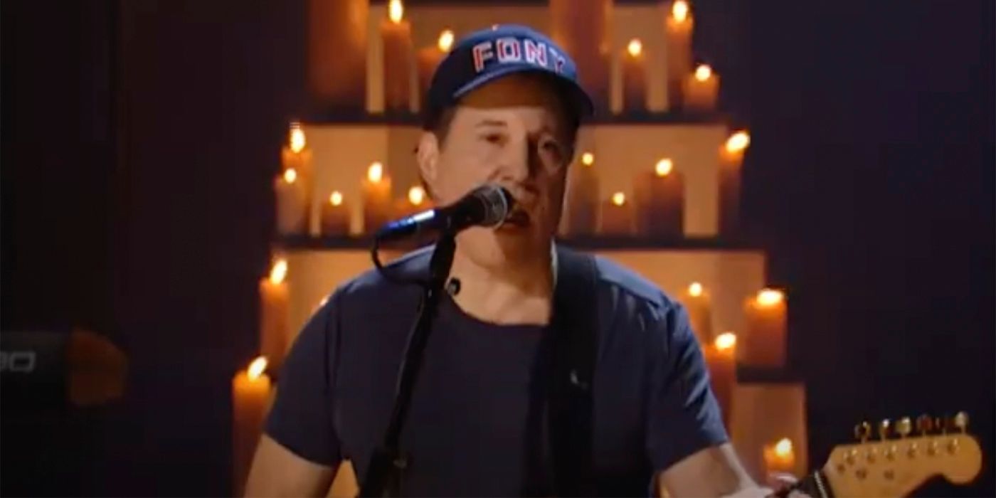 Paul Simon wearing an FDNY hat playing guitar with candles behind him on Saturday Night Live.