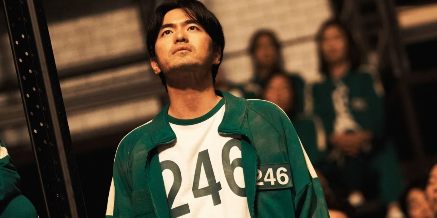 Player 246 looking up at something off-screen wearing a green and white signature Squid Game tournament tracksuit