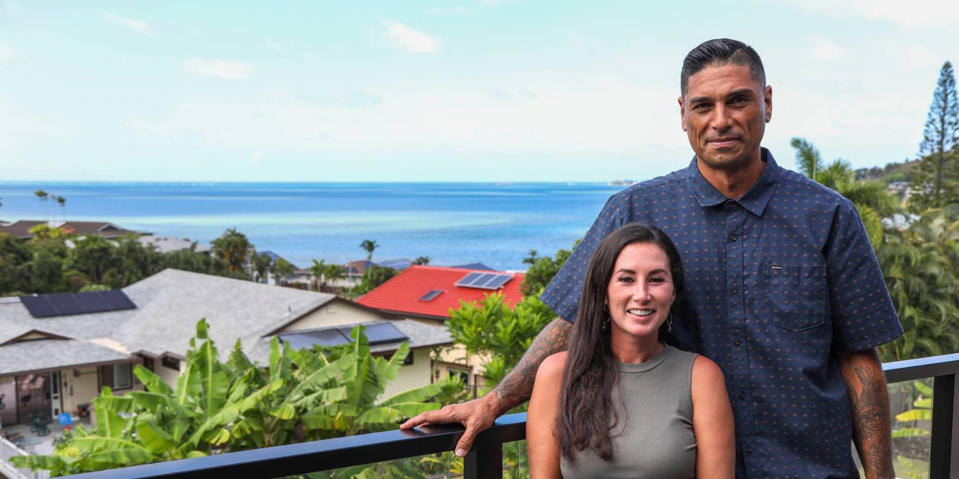 Tristyn and Kamohai Kalama on a balcony with a view of houses and palm trees behind them on Renovation Aloha.