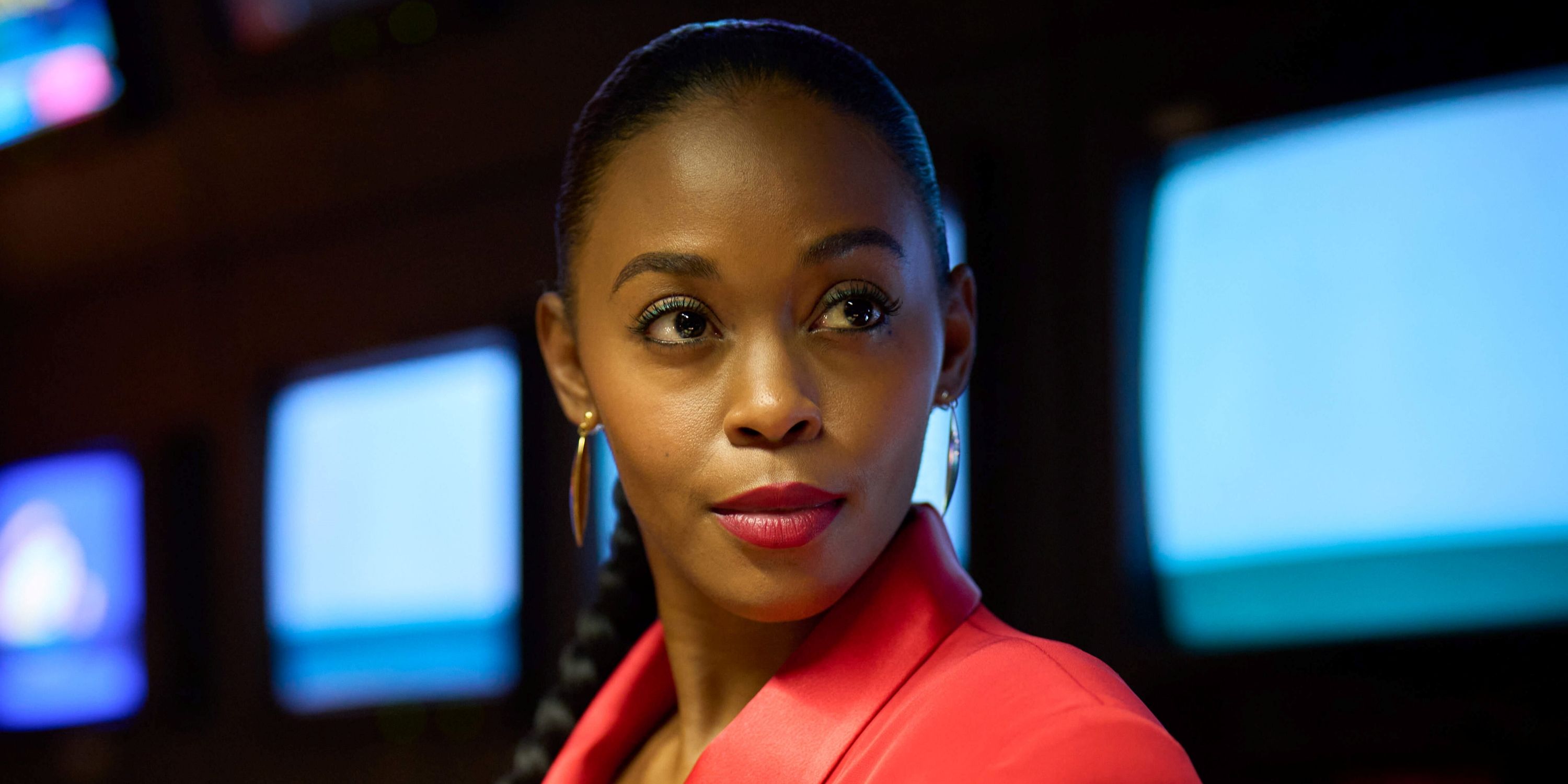 Nafessa Williams as Cameron Cook looking over her left shoulder in a red blazer in Rivals