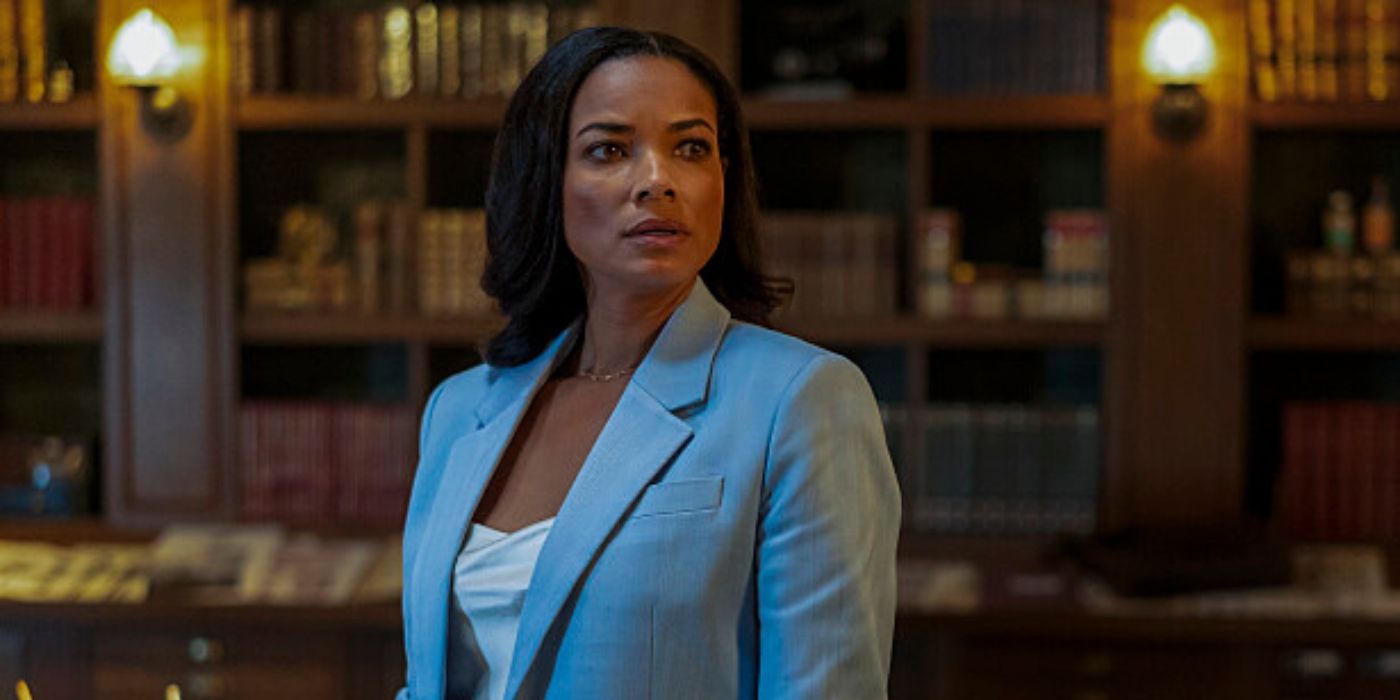 Rochelle Aytes as Dr. Mary Morstan in the CBS show Watson. She is standing in a warmly lit library, wearing a light blue blazer over a white top.