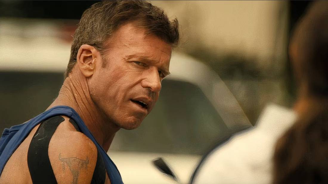 Taylor Sheridan as Cody Spears in a tanktop looking at someone to his right and talking to them in Lioness.