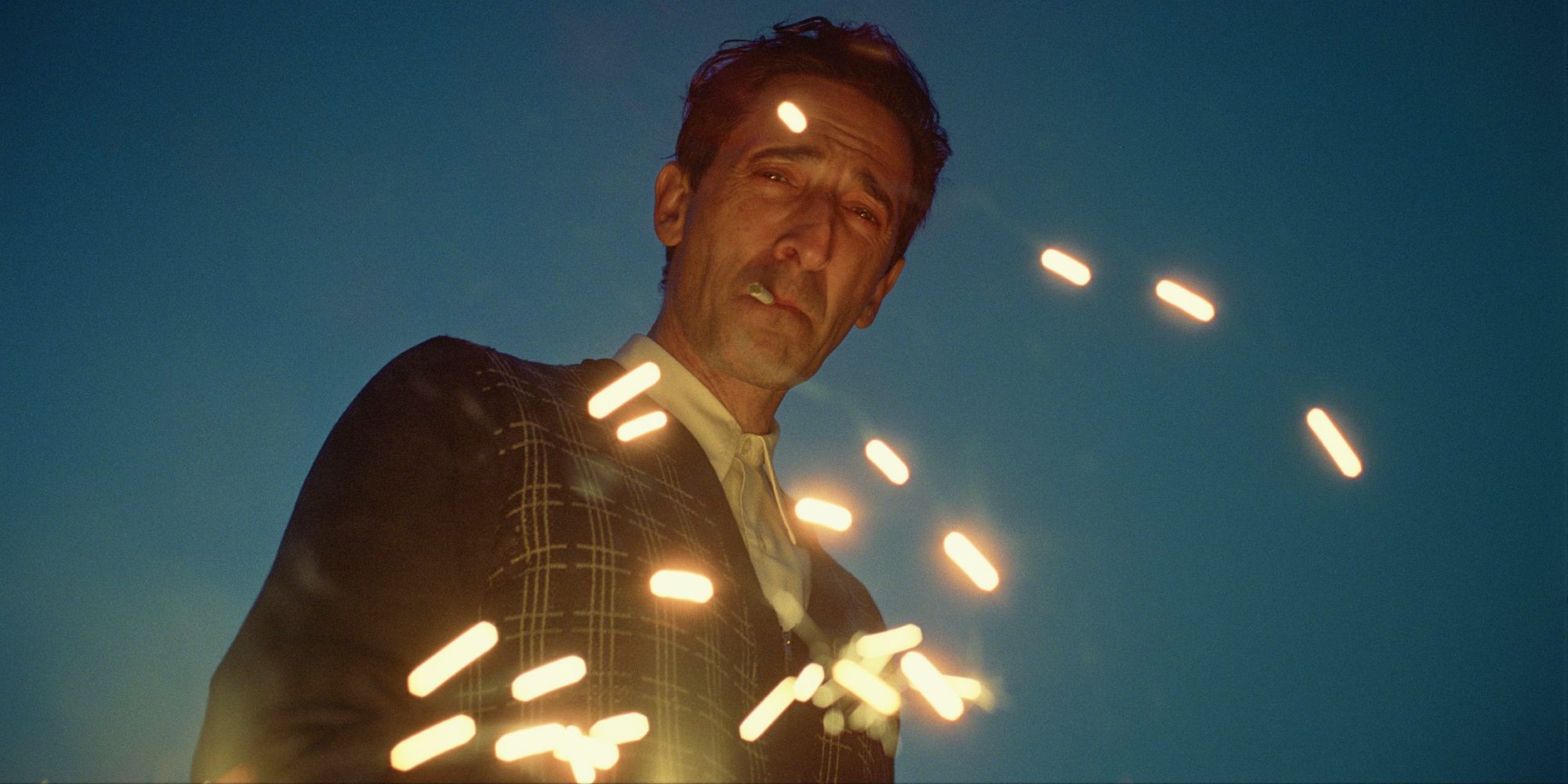 Adrien Brody staring at the ground with sparks rising in 'The Brutalist'