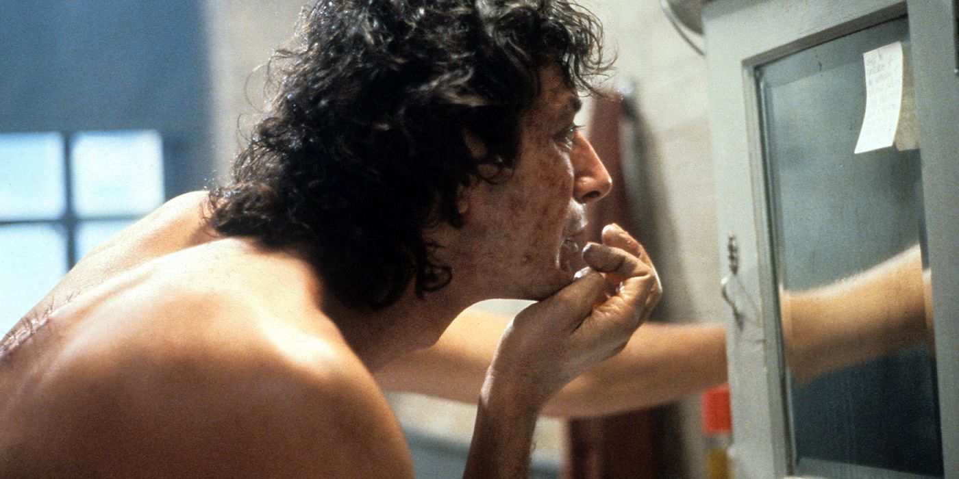 Seth Brundle (Jeff Goldblum) leaning close to a mirror examining himself in The Fly