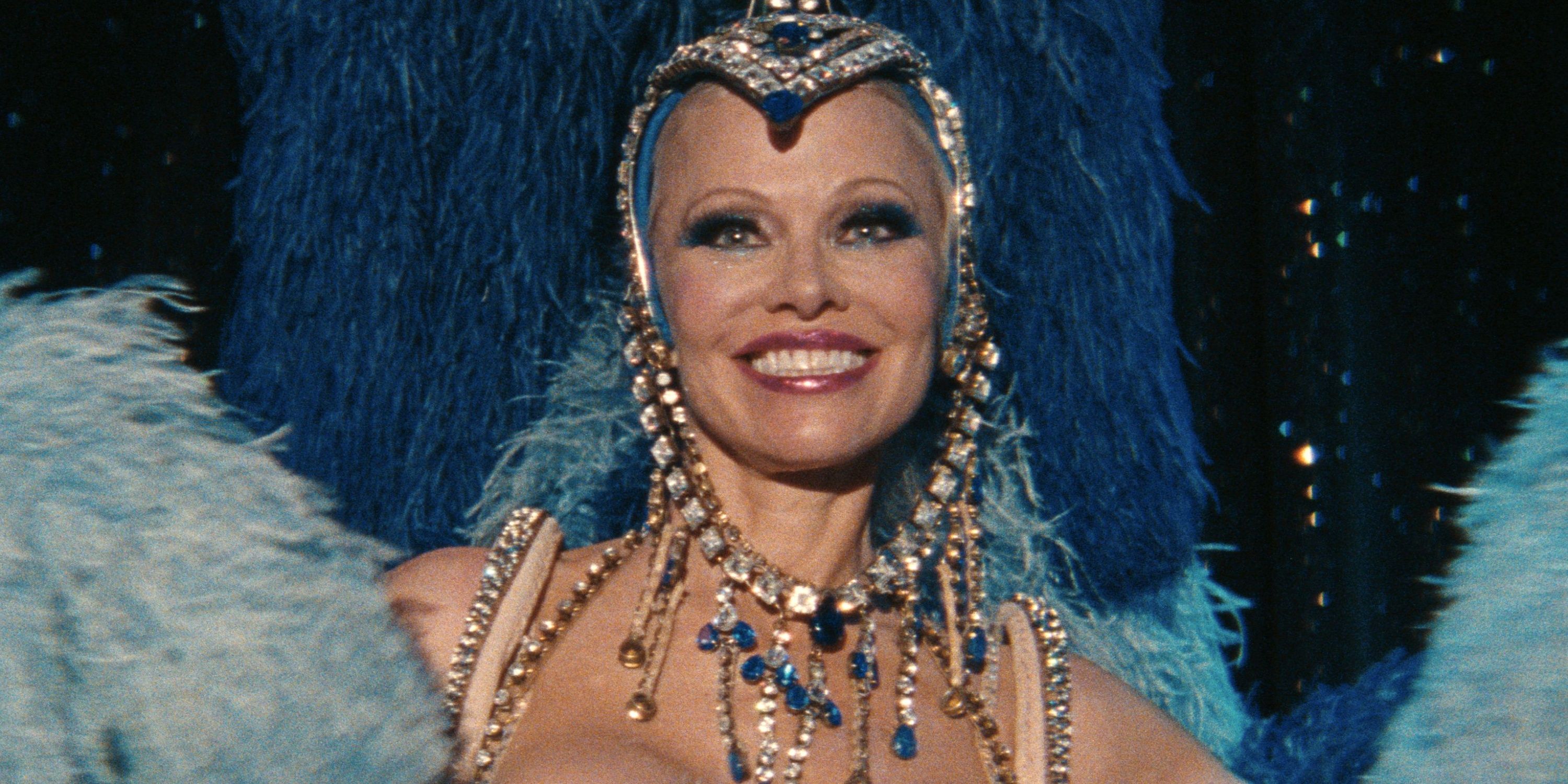 Pamela Anderson as Shelly in a showgirl costume with a dark blue feather headdress in The Last Showgirl