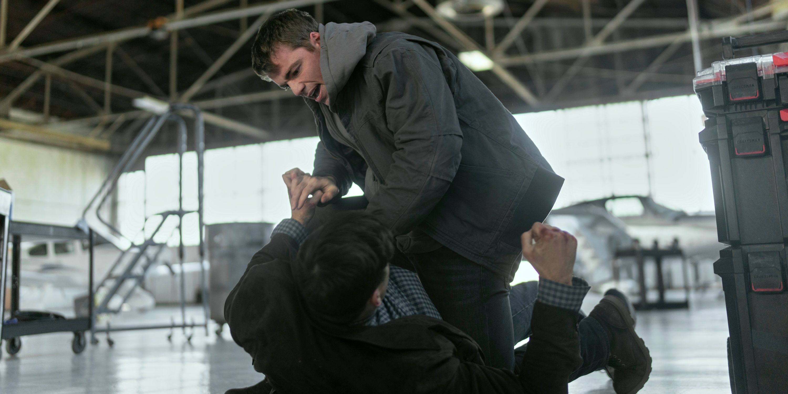 Gabriel Basso as Peter Sutherland fight someone while over them on the ground in Season 2 of The Night Agent
