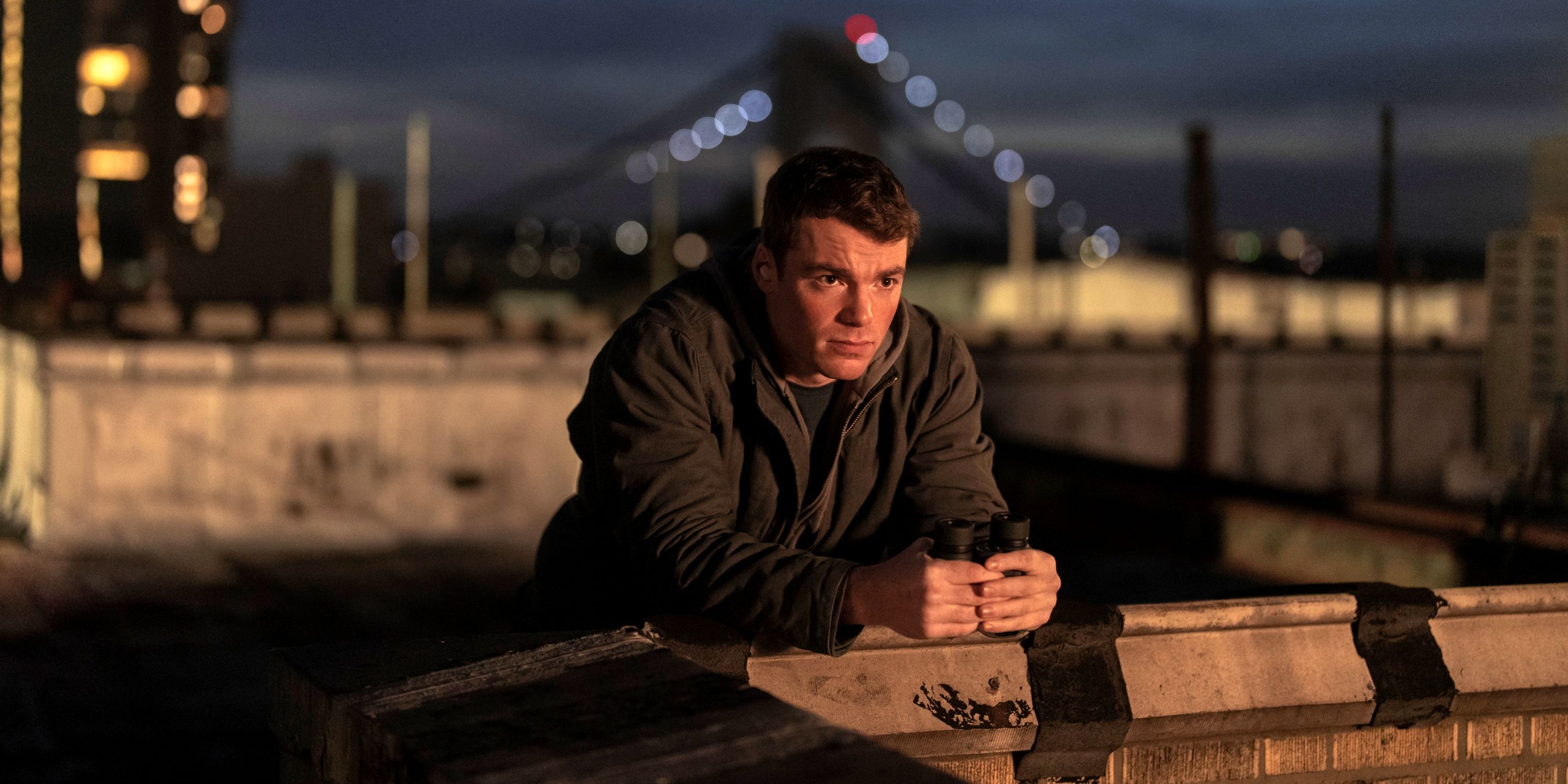 Gabriel Basso as Peter Sutherland leaning on a wall outside in Season 2 of The Night Agent