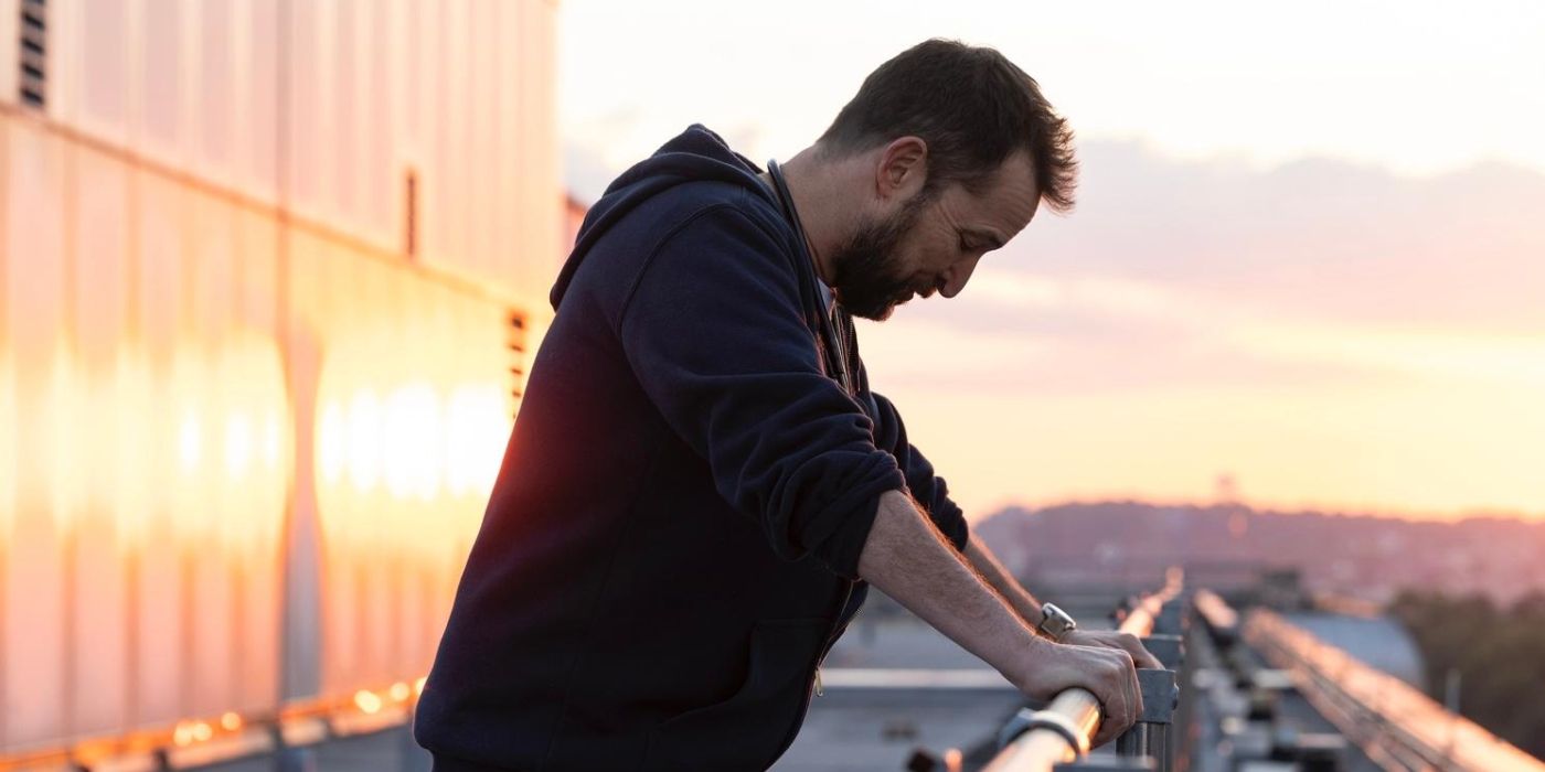 Dr. Robby (Noah Wyle) standing on the hospital roof and leaning against the railing as the sun rises in The Pitt