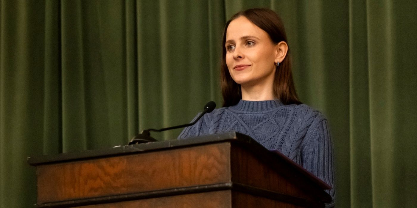 Pauline Chalamet as Kimberly standing at a podium in a blue sweater in The Sex Lives of College Girls