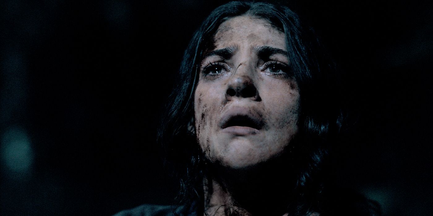 Clover (Ella Rubin) looking up in a dark room in fear with dirt and markings on her face