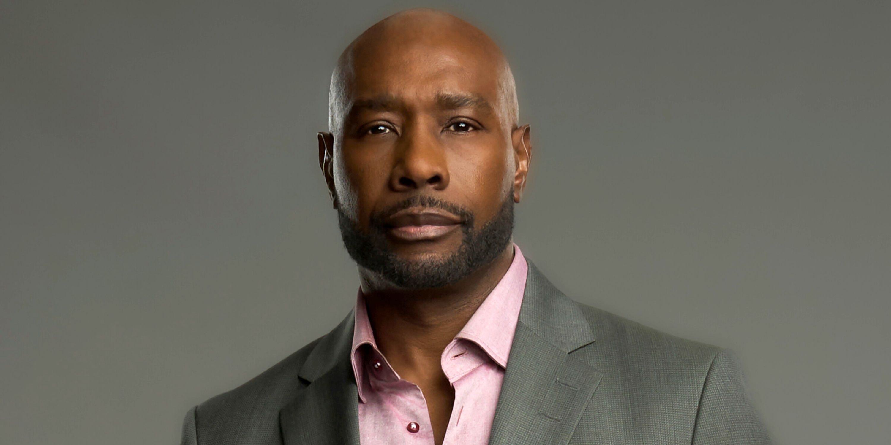 Morris Chestnut as Dr. Watson looking serious in a grey suit and pink shirt in a CBS promo shot for Watson