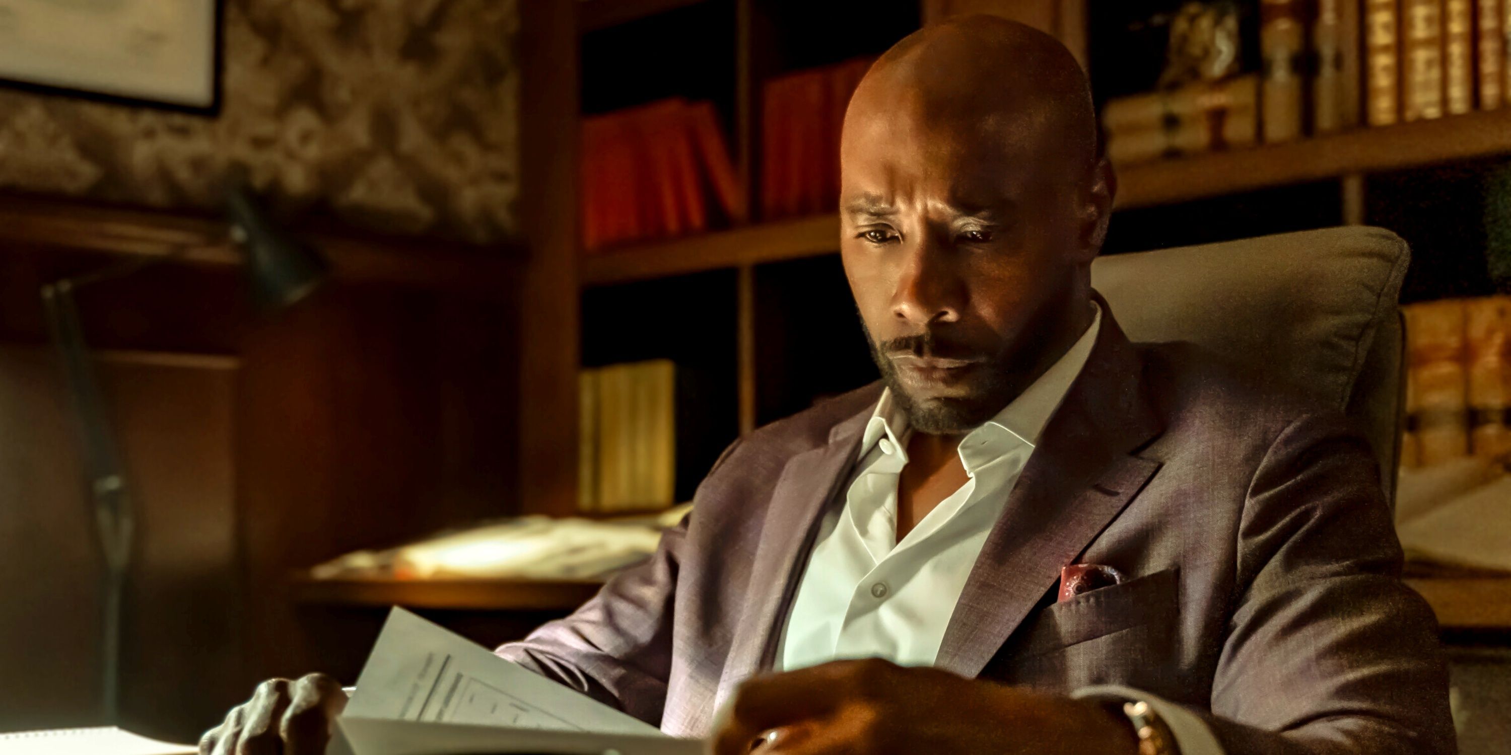 Morris Chestnut as Dr. Watson sitting at his desk looking at papers in the CBS series Watson