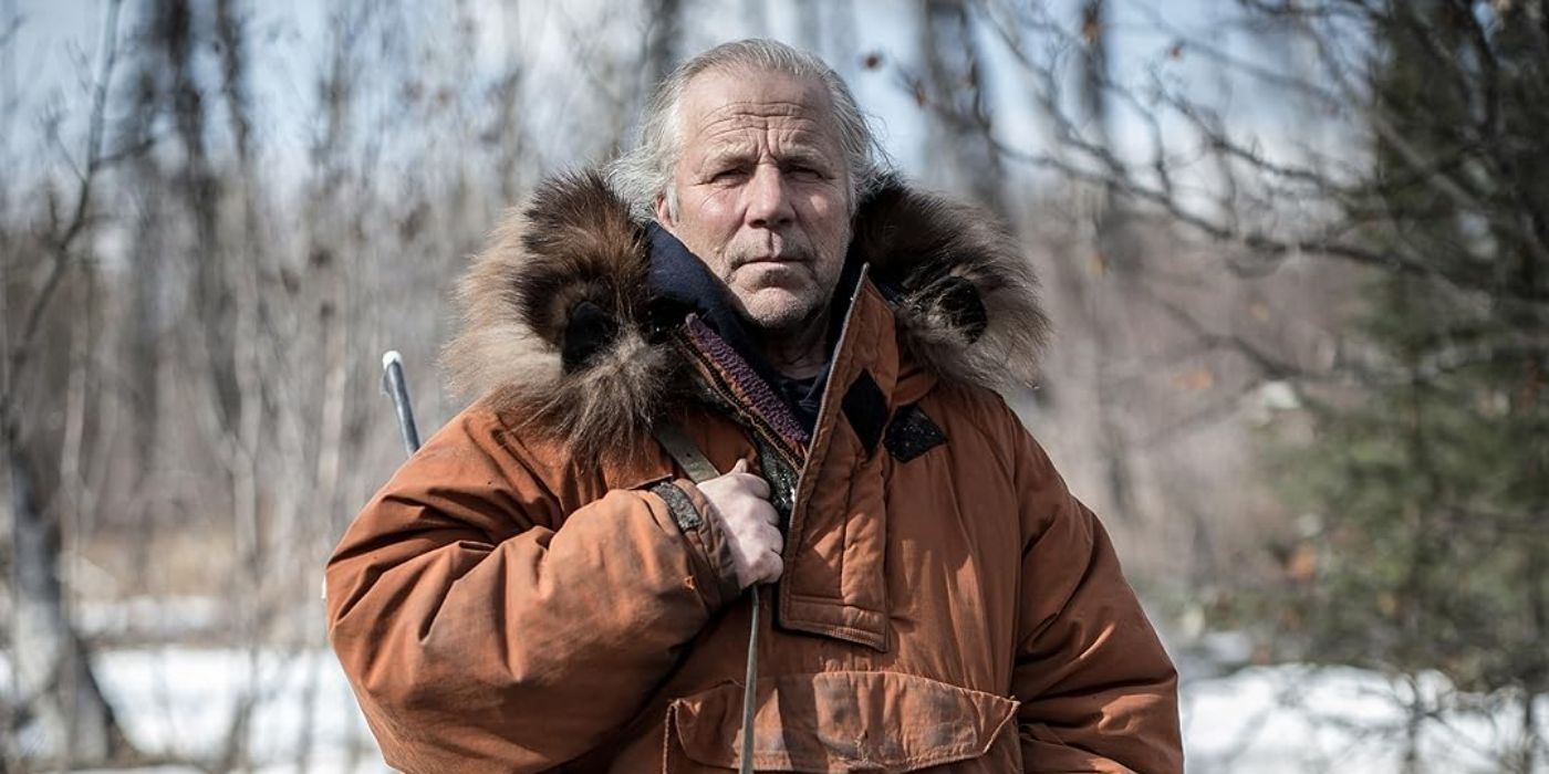 One of the castmembers of Yukon Men standing in the forest zipping his jacket up in an episode of Yukon Men.