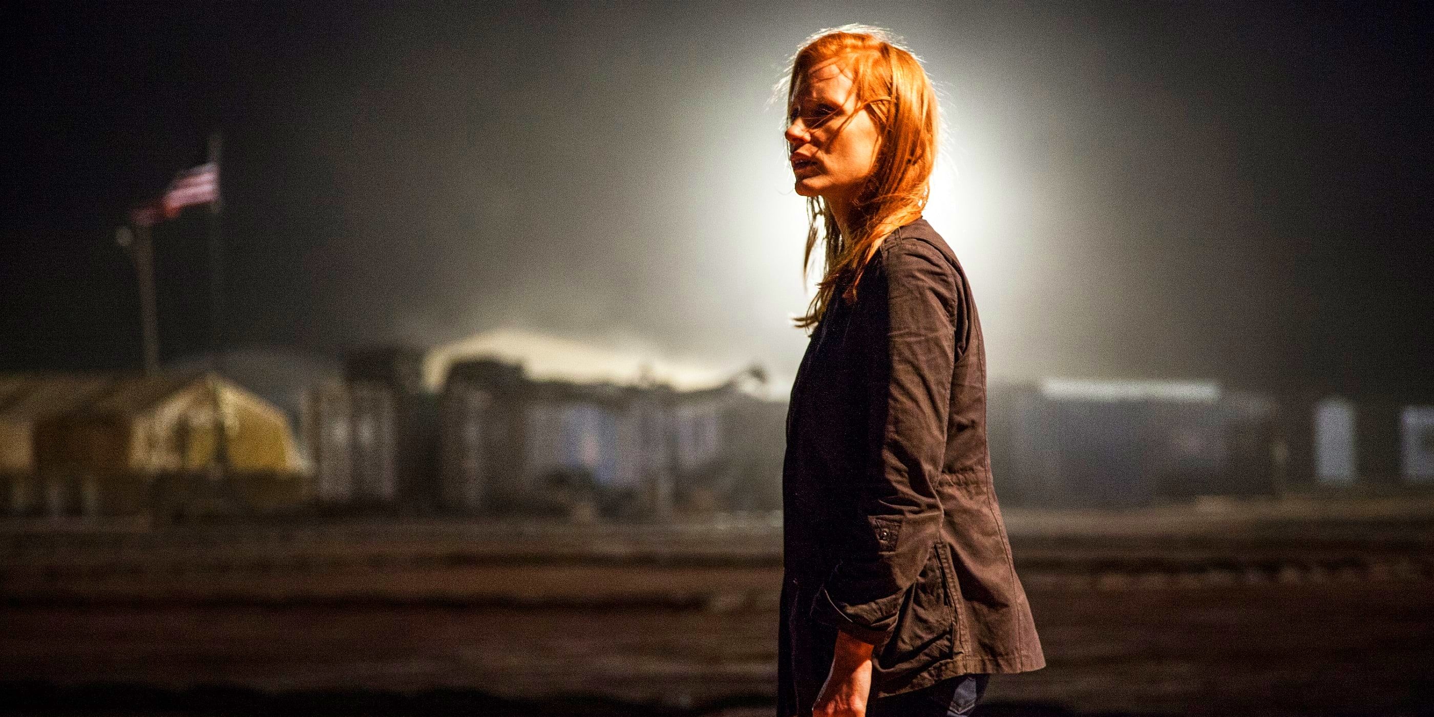 Maya, played by actor Jessica Chastain, stands stunned at night while a spotlight glows behind her head.