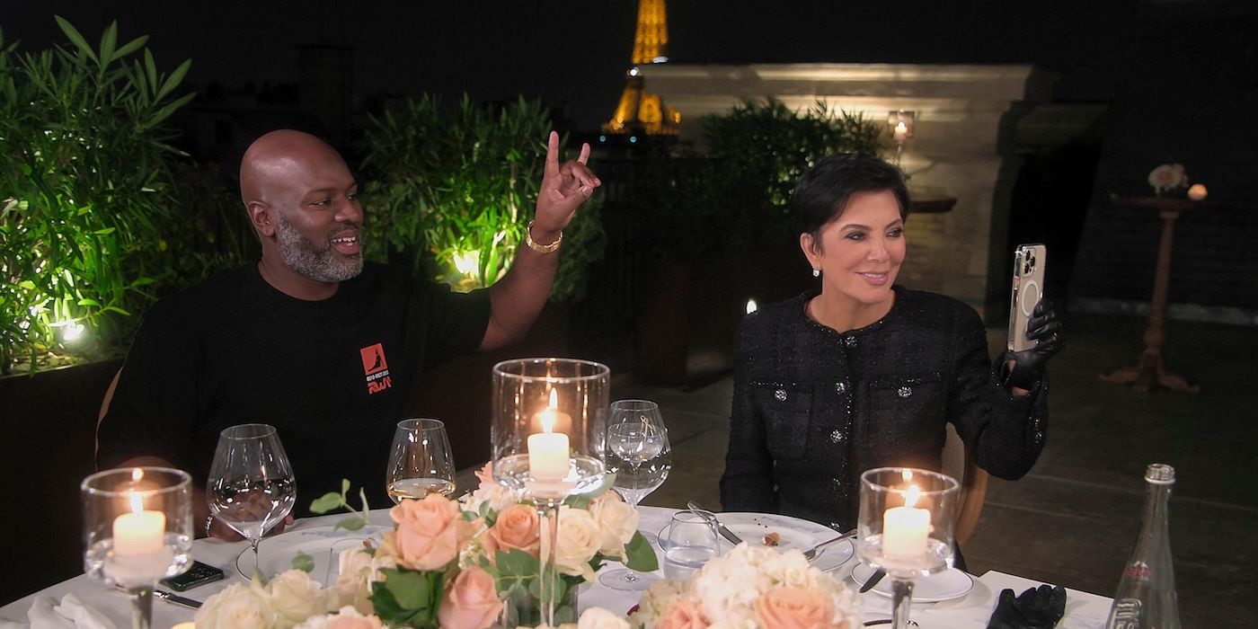 Corey Gamble signals horns with his hand as Kris Jenner records with her phone seated at a table on &lsquo;The Kardashians&rsquo;