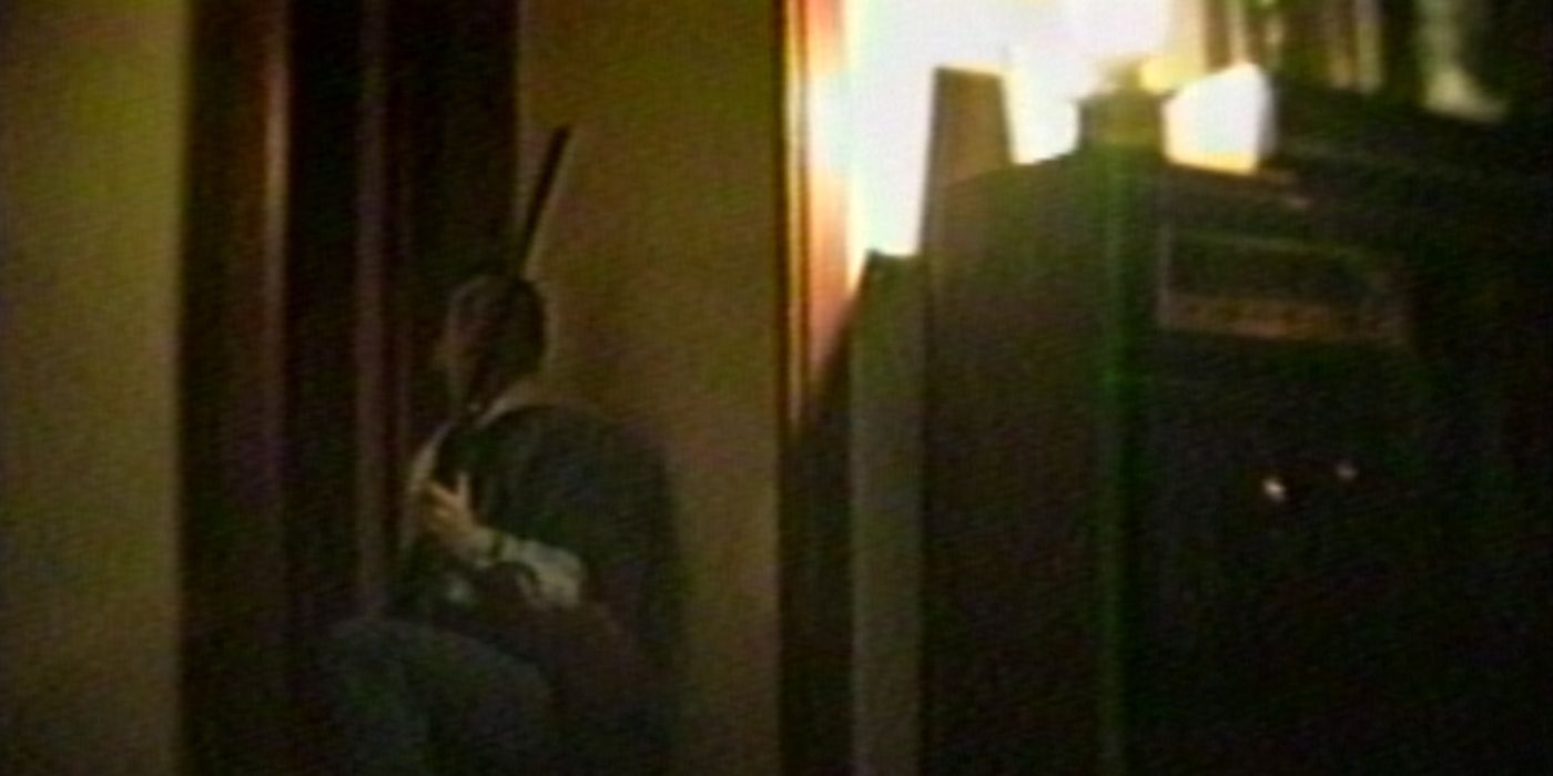 A man is crouching down behind a corner with a rifle in his hands as he waits for someone