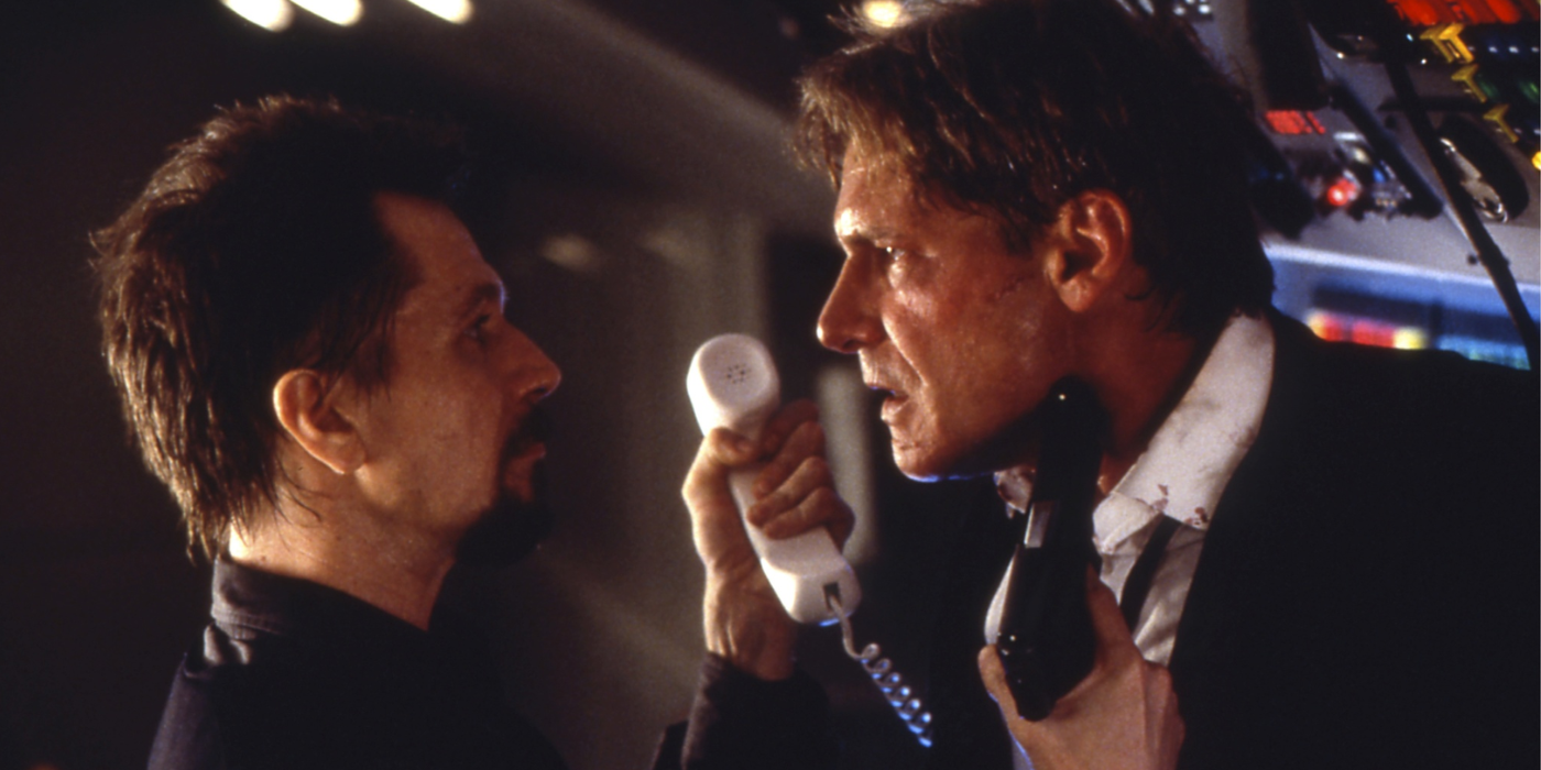 Gary Oldman threatens Harrison Ford with a gun as he holds up a phone in Air Force One.