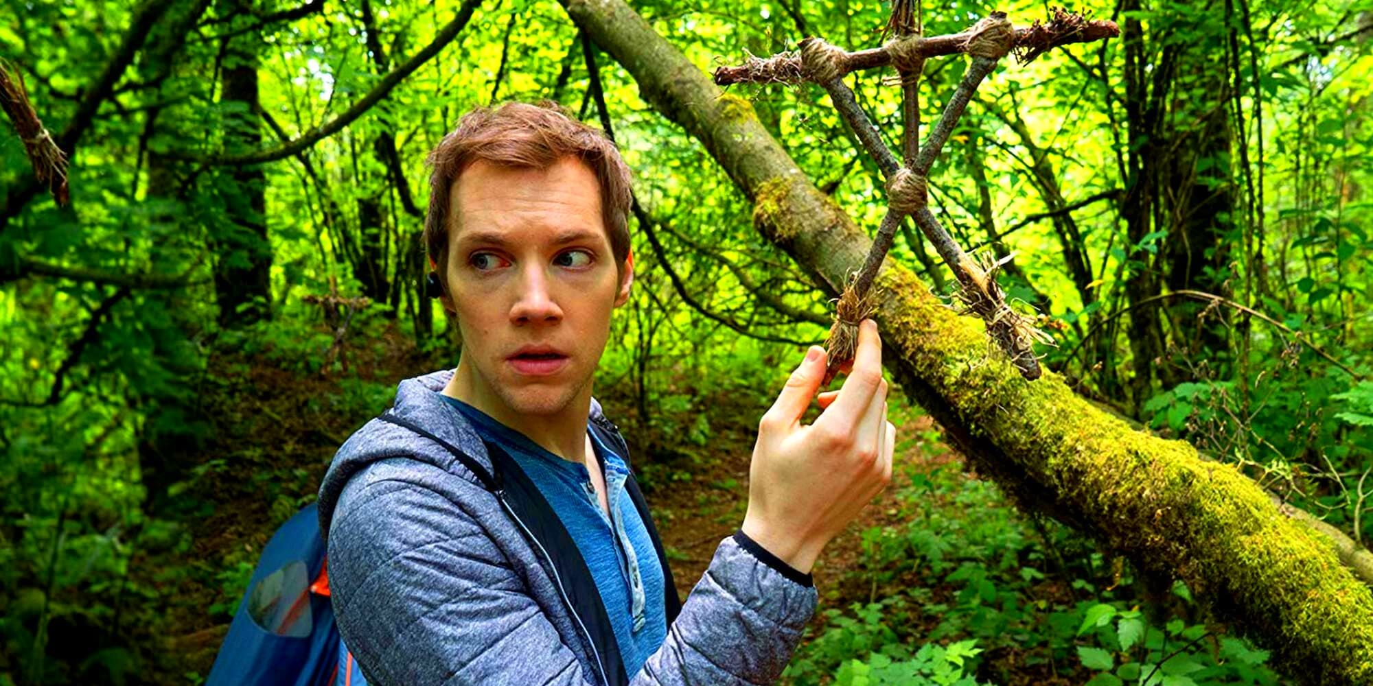 James Allen McCune comme James, dans les bois et tenant une figure de bâton suspendue à un arbre de Blair Witch.