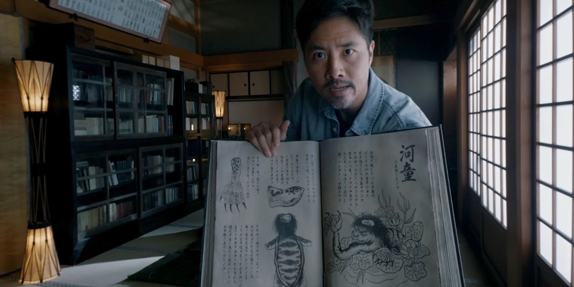 Kane Kosugi as Ryan holding up a book of folklore in Bloat