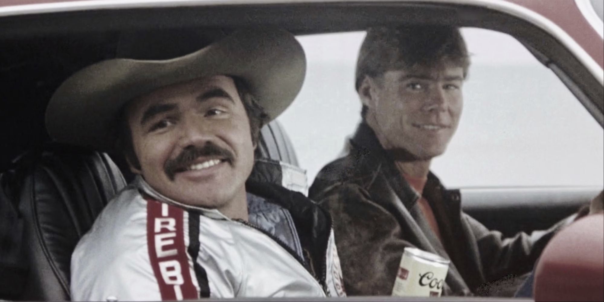 Burt Reynolds and Jan-Michael Vincent looking out the window of a car and smiling in Hooper.