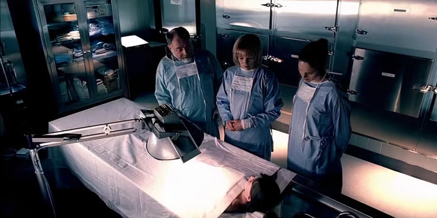 Three agents wearing scrubs stand in a morgue looking over a dead body in CSI.
