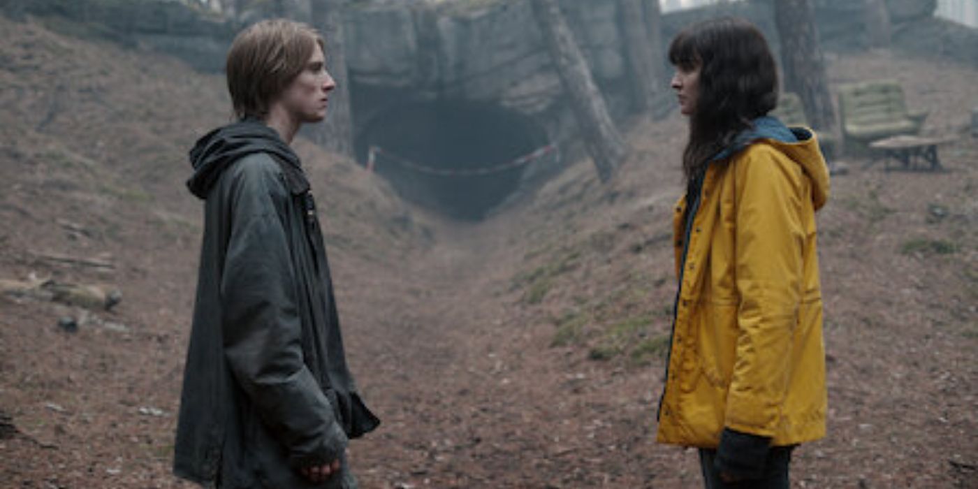 A man and woman wearing raincoats face each other, standing in the forest in Dark.