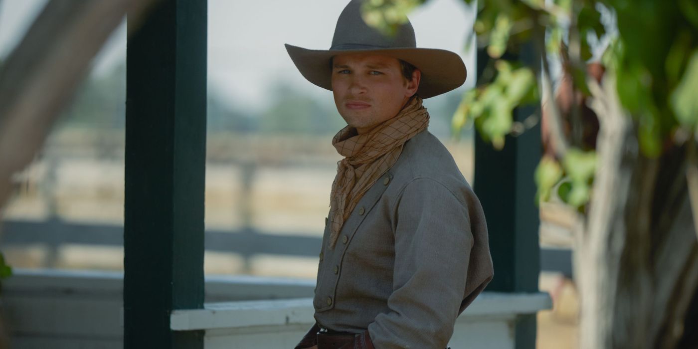 Darren Mann as Jack Dutton in cowboy garb with a cowboy hat is looking to his left, towards the camera in1923.