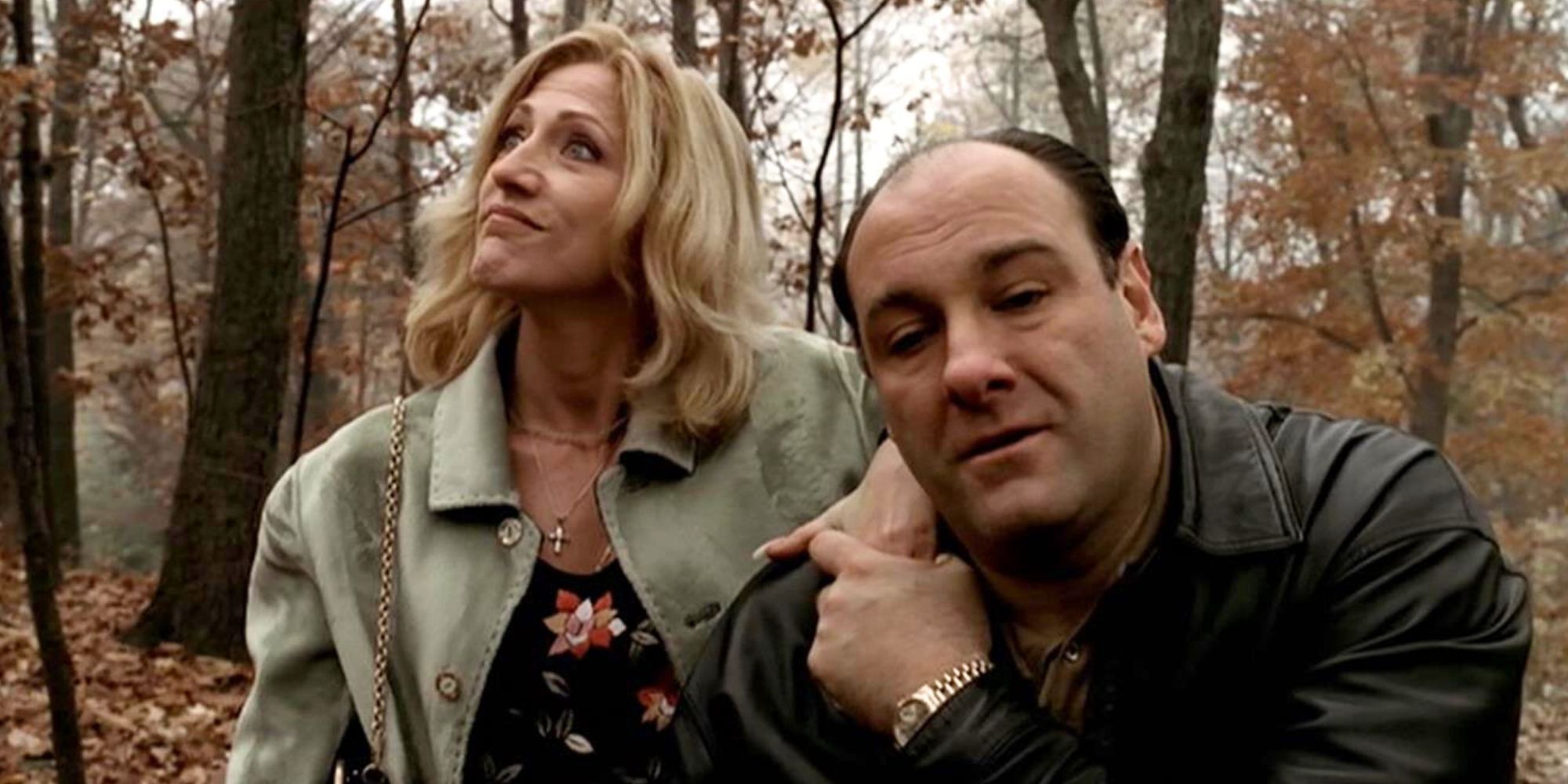 Edie Falco is behind James Gandolfini as he holds her hand on his shoulder in the woods in The Sopranos.