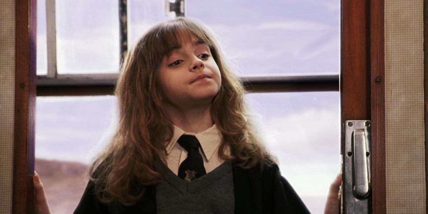 Hermione (Emma Watson) standing in between train carriage doors, looking down while her chin is raised.