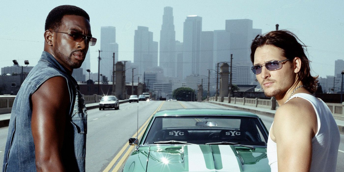 Two men stand in front of a sports car and look back with sunglasses on in Fastlane.