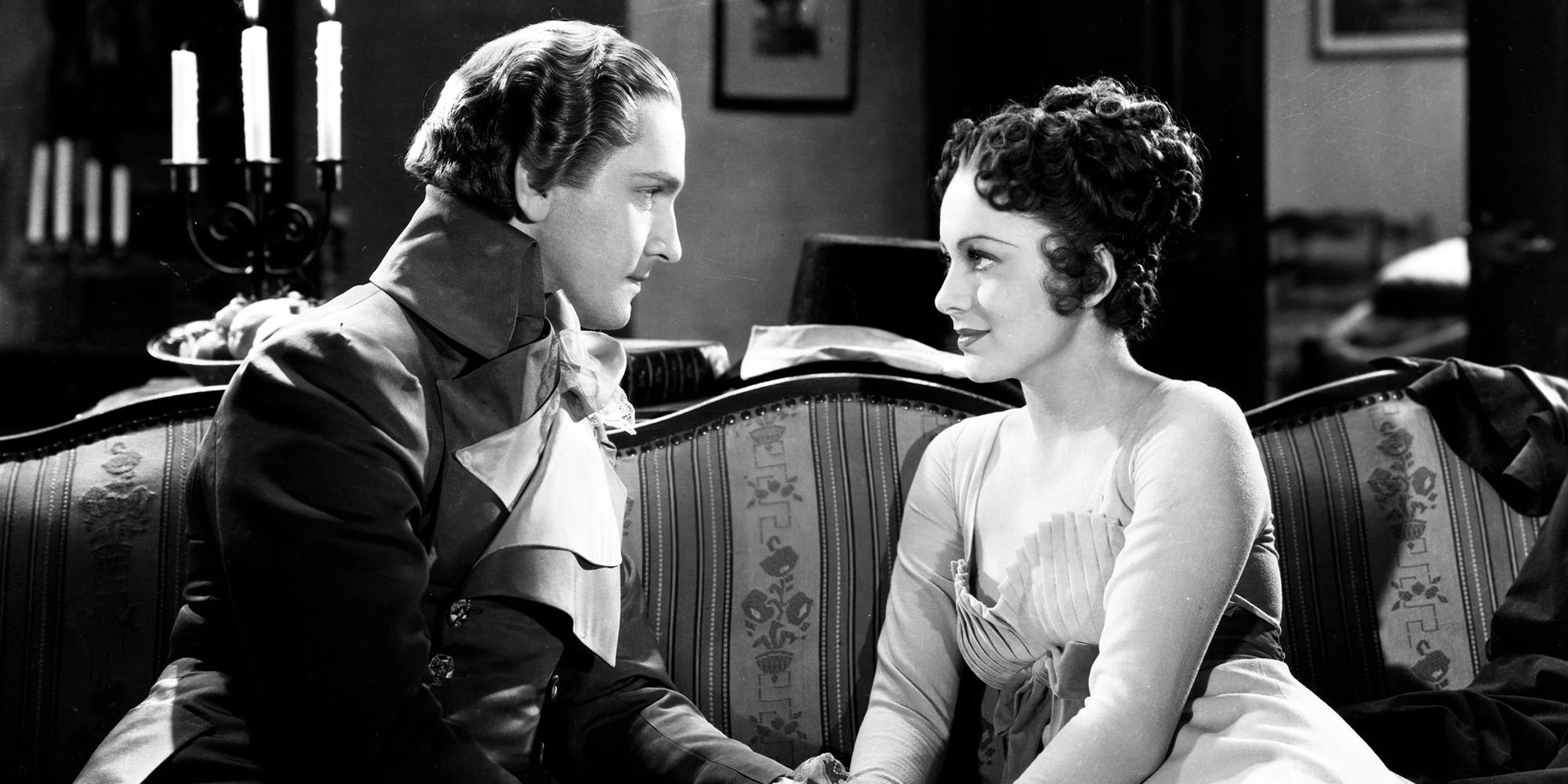 Fredric March and Olivia de Havilland in 'Anthony Adverse', looking at each other on a couch