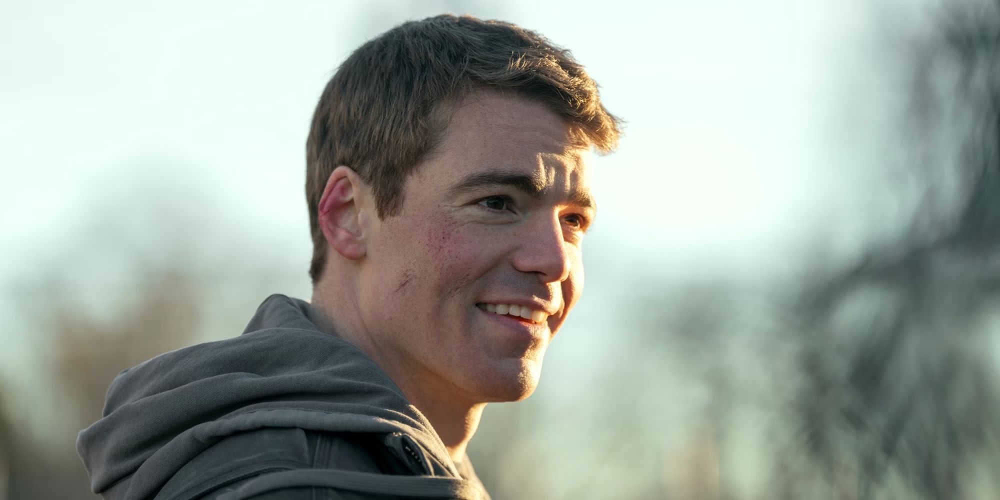 Gabriel Basso as Peter smiling while looking over his right shoulder in Season 2 of The Night Agent.