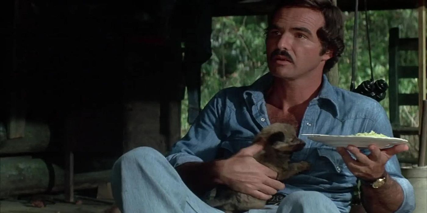 Burt Reynolds as Gator holds a plate of food with an animal in his lap in Gator.