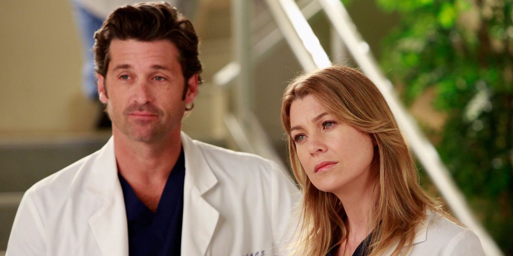 Meredith and Derek in doctors' coats look at something off-screen in Grey's Anatomy.