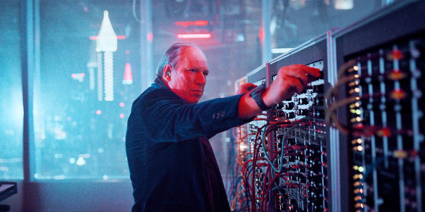 Hans Zimmer adjusting dials on a soundboard in front of a window of a city skyline