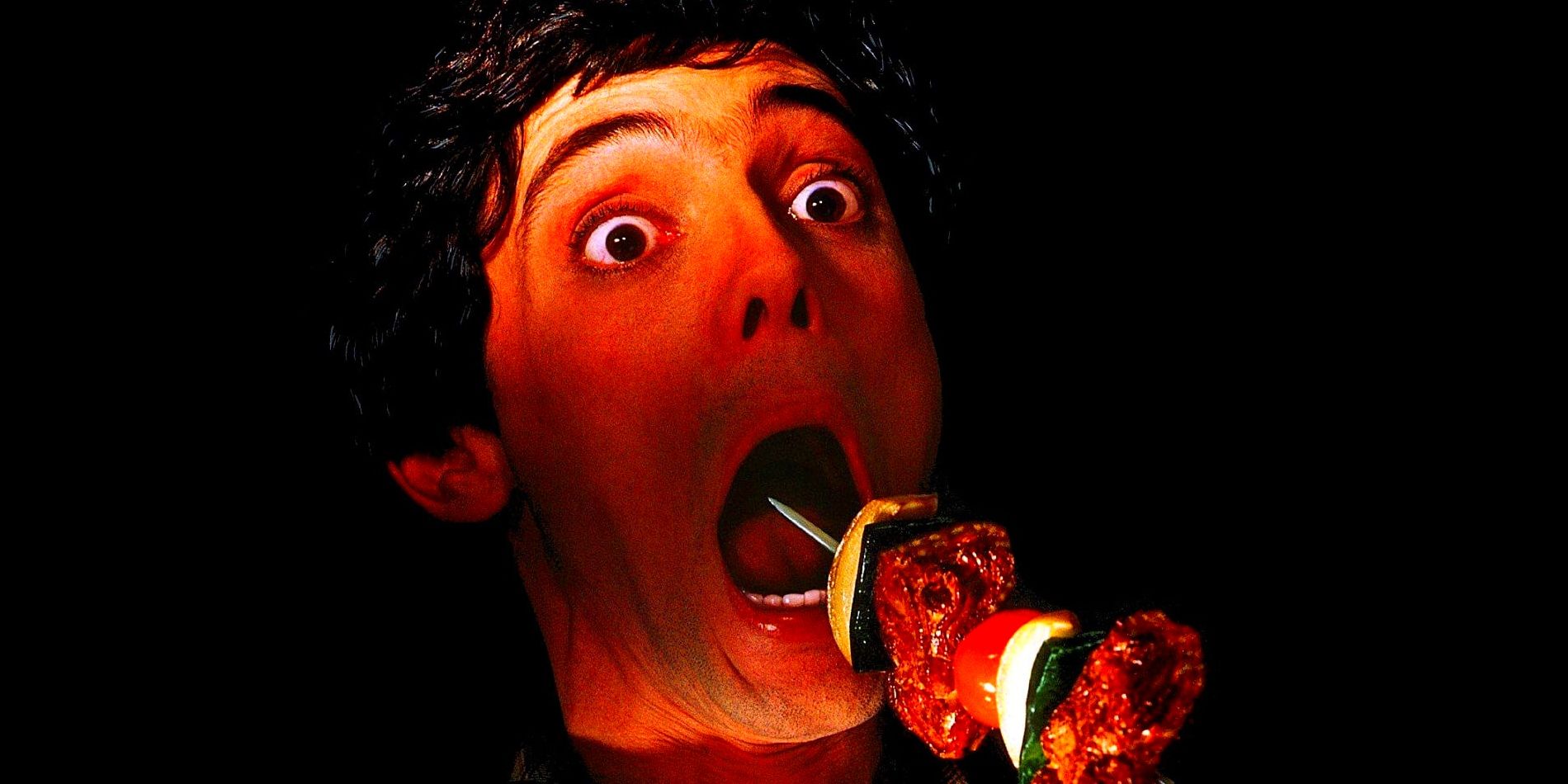 A dark-haired man opens his mouth in a scream while a skewer with meat and vegetables on it is driven towards his face.