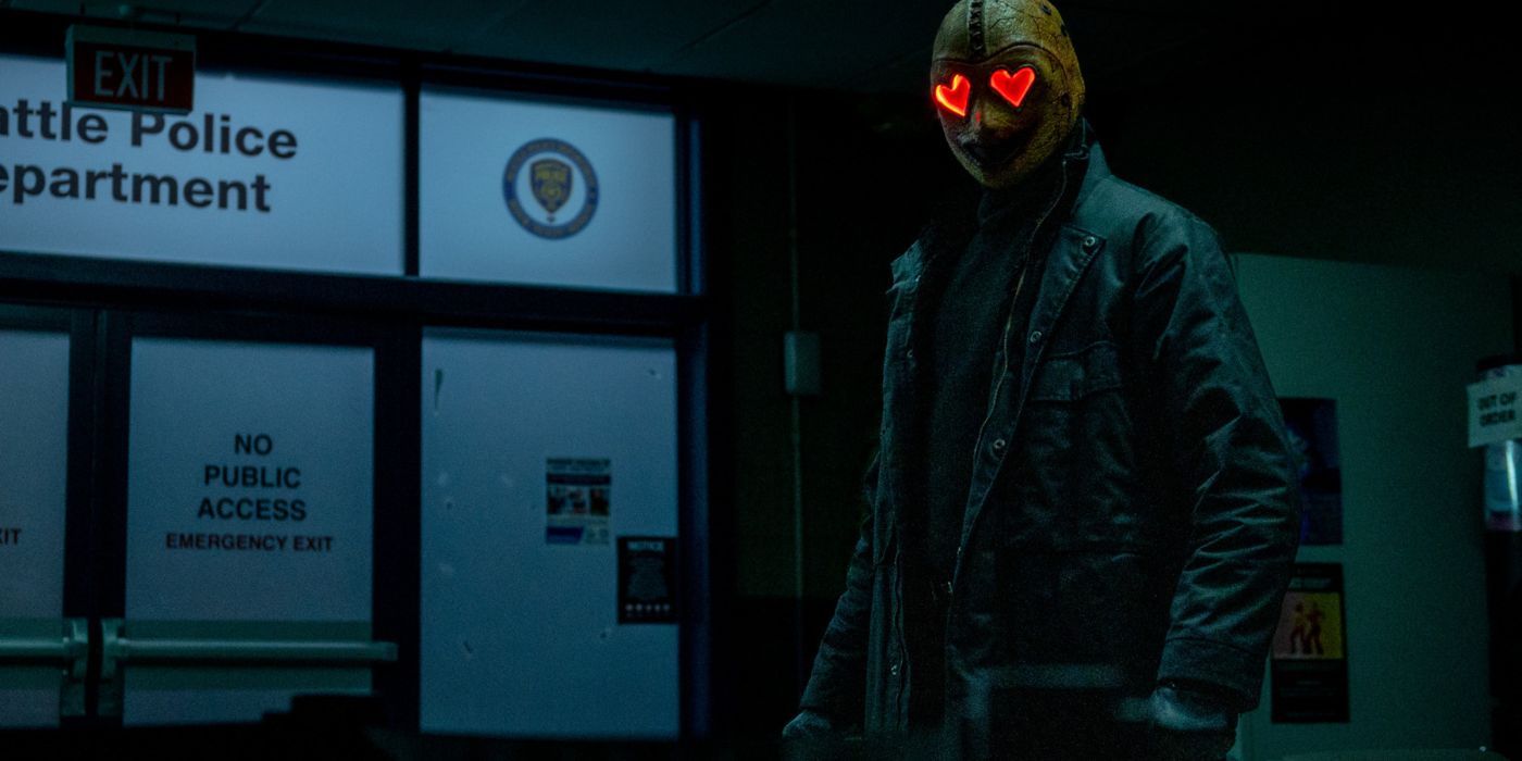 HEK stands at the entrance of the police station, mask eyes glowing in a blackout in Heart Eyes.