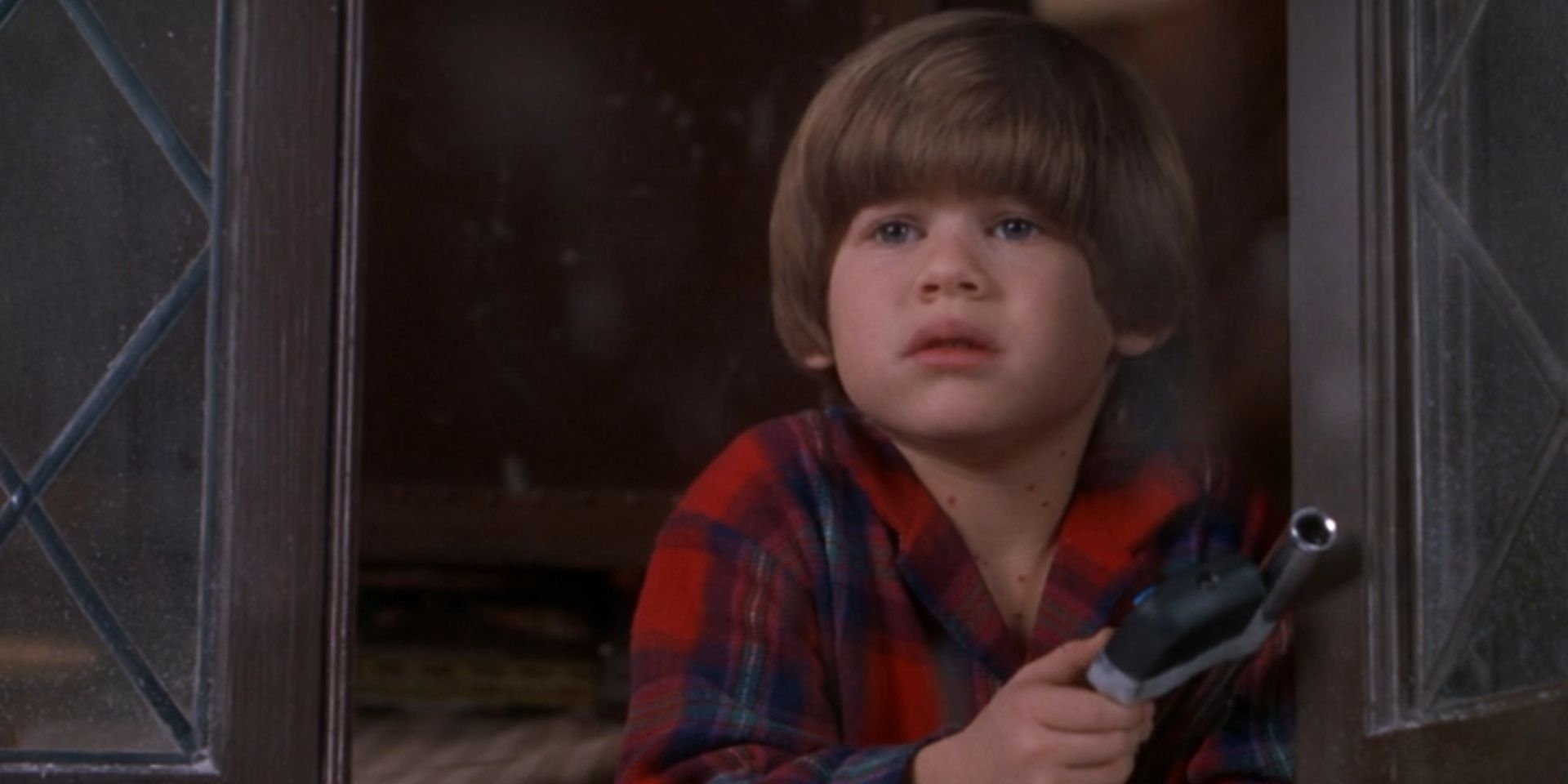 Alex Pruitt, played by Alex D. Linz, looks out a window while holding a TV remote in 'Home Alone 3'.