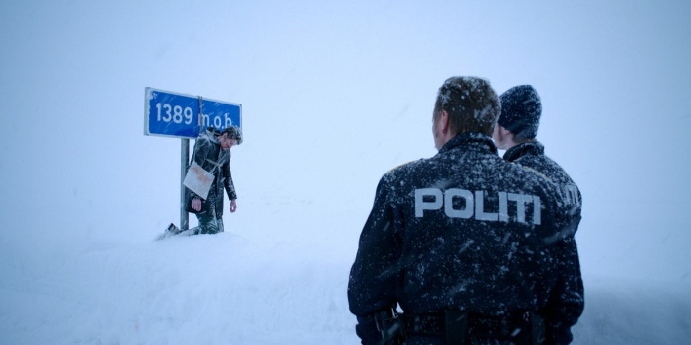 Two police officers stand in the snow and look at a body tied to a road sign