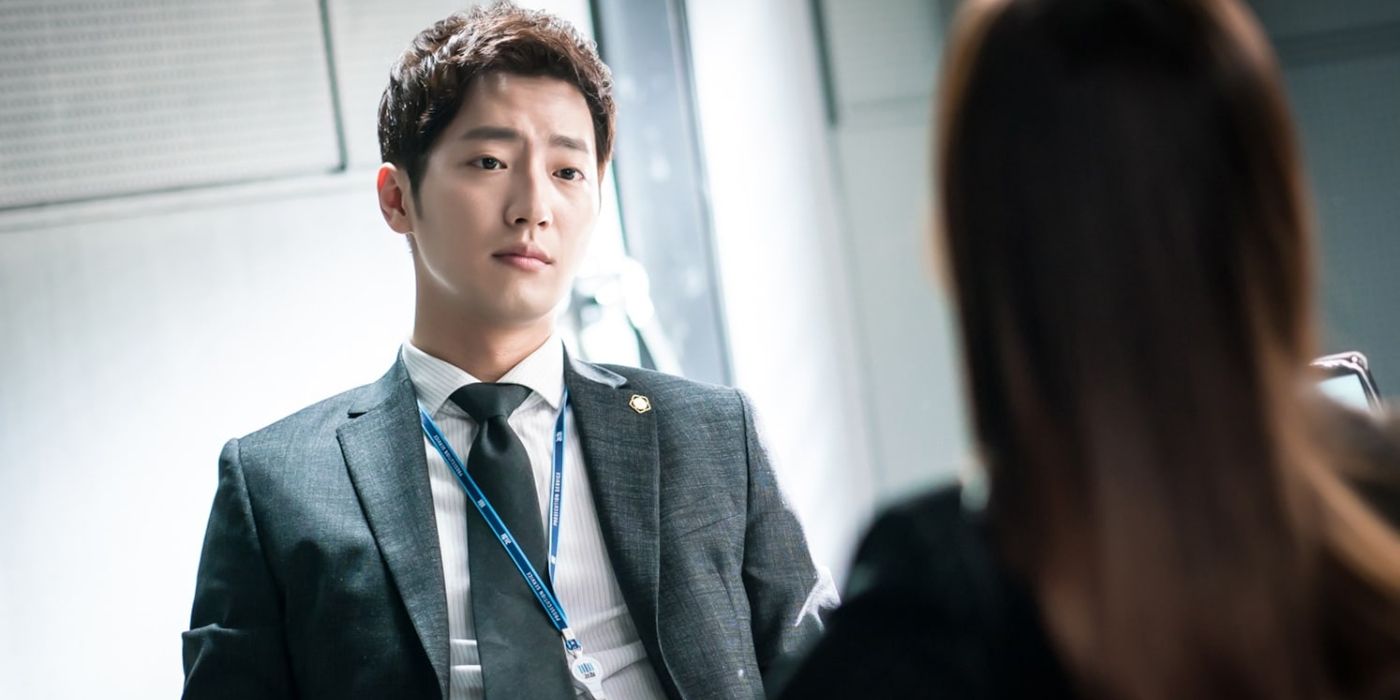 Lee Sang-yeob as Lee Yoo-beom in a suit sits across from a woman and looks worried in?While You Were Sleeping.