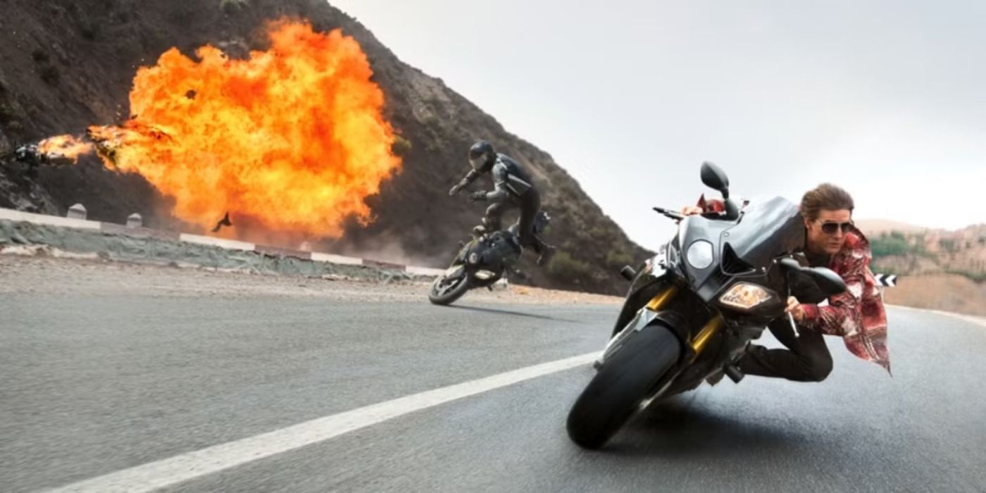 Tom Cruise as Ethan Hunt on a motorcycle with an explosion nearby in Mission Impossible Rogue Nation.