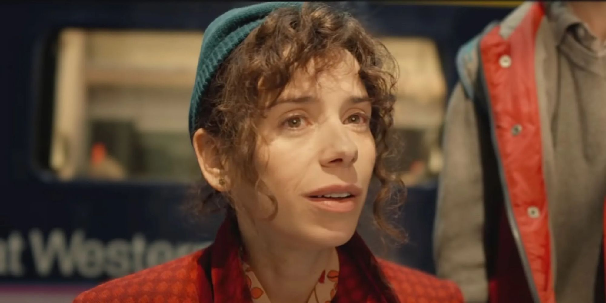 Mrs. Brown (Sally Hawkins) in a hat and coat looks amused at something in the Paddington films.