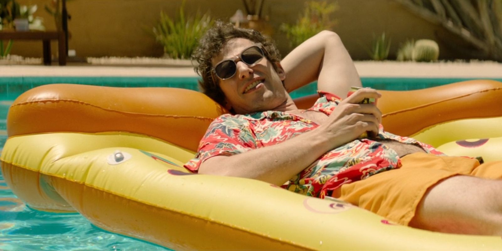 Nyles, played by Andy Samberg, floats in a pool on an inflatable pizza in 'Palm Springs'.