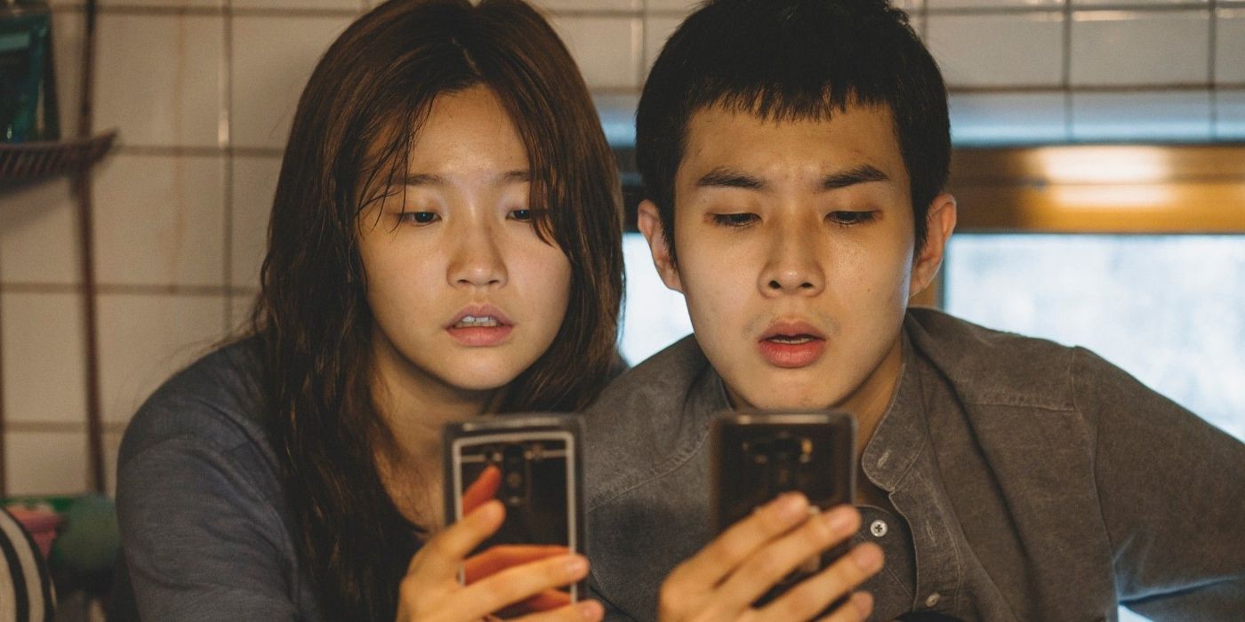 Park So-dam and Choi Woo-shik check their cellphones in a scene from Parasite
